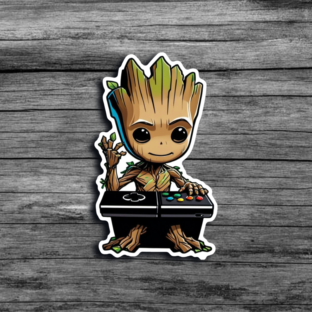 A sticker of Baby Groot sitting at a DJ booth like table, with Xbox/Playstation buttons, with one hand raised