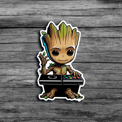 A sticker of Baby Groot sitting at a DJ booth like table, with Xbox/Playstation buttons, with one hand raised