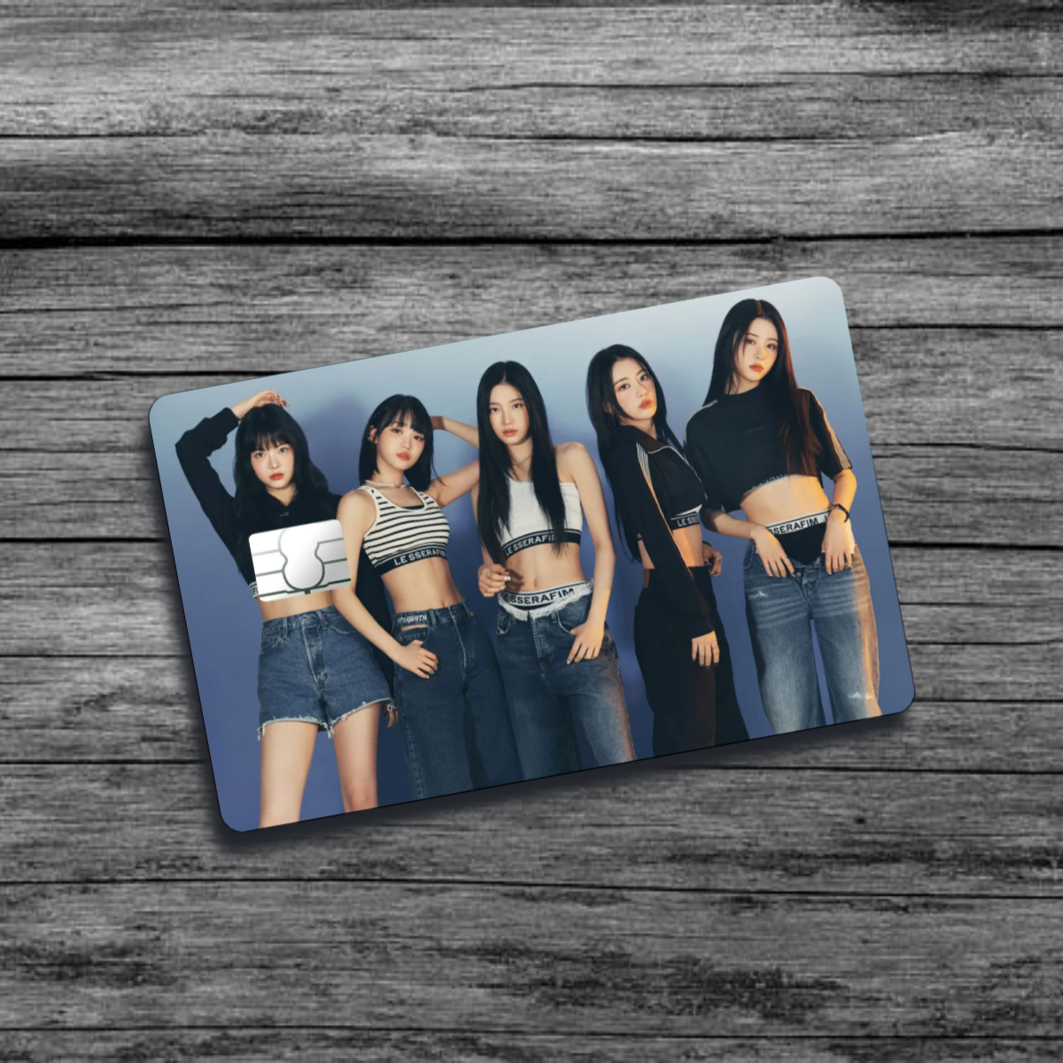 A credit card skin featuring K-Pop group Le Sserafim, five stylish women wearing jean clothing and crop tops, set against a blue-ish gray background.
