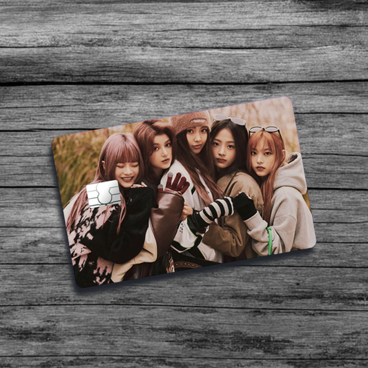 A credit card skin featuring K-Pop group New Jeans, five stylish women with wearing sweatshirts and winter/fall apparel, in a field.