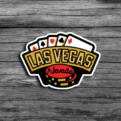 A sticker of a Las Vegas sign with two chips with "Nevada" printed on them, and a few cards behind the sign